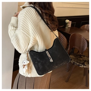 Detail of a minimalist black shoulder bag with a silver metal clasp and a bear charm