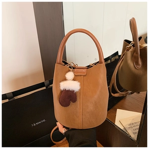 Detail of vintage caramel suede bucket bag with vertical stitching and plush charm