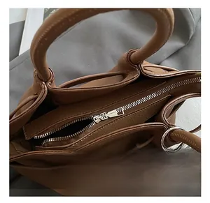 Detail of a brown leather bucket bag with silver zipper and plush pom-pom charm