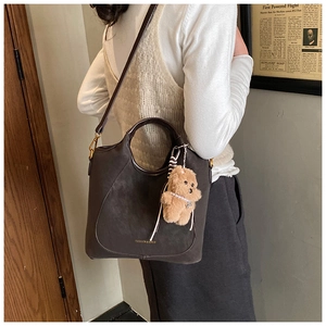 Detail of retro suede bucket bag with leather strap and plush bear charm on a model