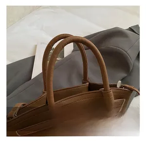 Close-up of brown leather bucket bag showing dual cylindrical handles and silver metal rings