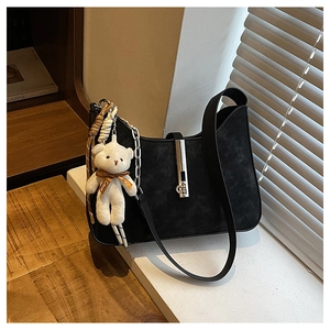 Detail of black suede shoulder bag with silver buckle and cute teddy bear plush charm
