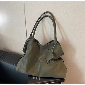 Detail view of dark green tote bag featuring white contrast stitching and a star charm accessory