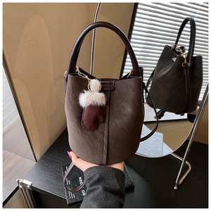 Macro view of dark brown suede bucket bag with leather trim and glove-shaped charm