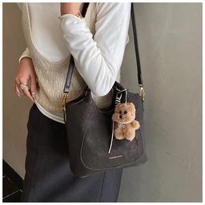 Detail of dark matte shoulder bag with gold hardware and a cute plush bear charm