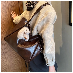 Detail of soft dark brown leather tote bag featuring a cute plush bunny charm pendant