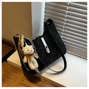 Macro detail of black suede shoulder bag featuring silver metal clasp and a bear charm