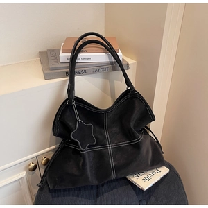 Detail of black leather tote bag with white contrast stitching and star charm pendant