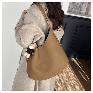 Détail du sac bandoulière en cuir caramel avec boucle dorée et pendentif ours