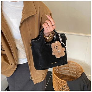 Detail of black matte tote bag with golden logo lettering and a brown plush bear charm