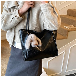 Detail of black glossy faux leather tote bag with soft texture and plush bunny charm