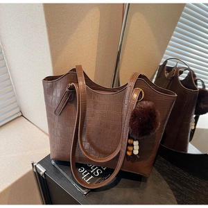 Detail of dark brown faux crocodile bucket bag with decorative pompom and mirror reflection