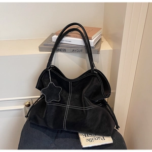 Detail view of black tote bag with white contrast stitching and a star charm