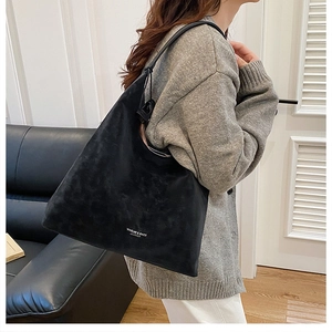 Details einer schwarzen Schultertasche aus mattem Wildleder mit weißem Logo-Aufdruck