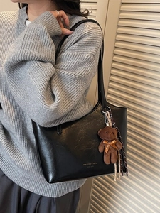 Retro black leather tote bag with bear charm and gold logo on grey sweater