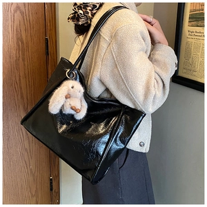 Detail of black faux leather tote bag with glossy finish and cute plush bunny charm