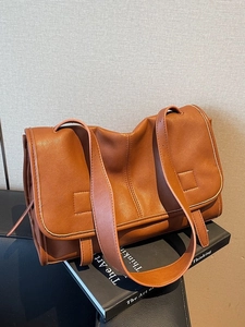 Brown leather messenger bag with flap closure on a decorative book, stylish shoulder bag