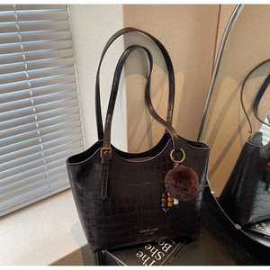 Detail of dark brown crocodile pattern bucket bag with fur pompom and brand logo