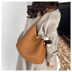 Sac cabas en cuir marron avec un pendentif ours en peluche porté avec un manteau gris en laine