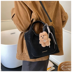 Close-up of black leather bucket bag with teddy bear pendant and woven strap details