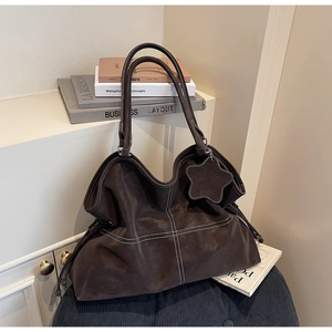 Detail of dark brown tote bag with white contrast stitching and star pendant on blue stool