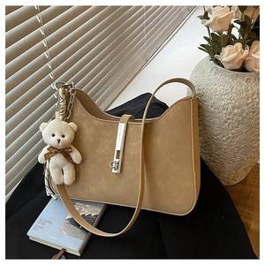 Close-up of camel suede crescent bag with silver latch and plush bear charm detail
