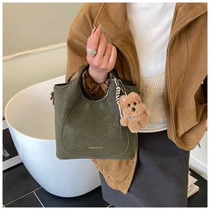 Detail view of dark green leather bucket bag featuring fashion text and plush bear charm