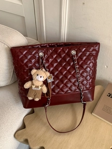 Burgundy quilted tote bag with silver chain strap and cute bear charm on a desk