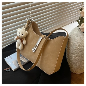 Detail of beige suede underarm bag with silver buckle and plush bear charm on black blazer