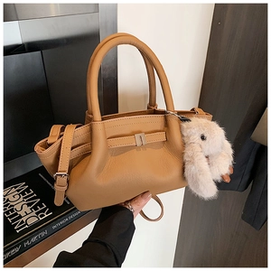 Close-up of tan lychee-grain bucket bag with plush bunny charm and top handle