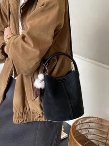 Retro black faux suede bucket bag with round handle and plush charm, shown on model