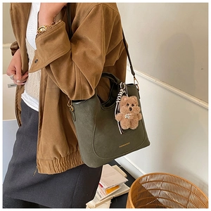 Detail of dark green bucket bag with a cute bear charm and gold lettering on matte leather