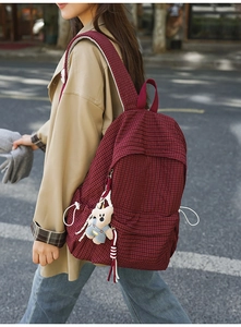 Detail of red plaid backpack with plush bear charm worn by a model in autumn coat