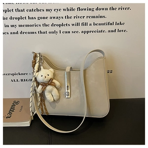 Detail view of beige faux leather underarm bag with silver buckle and plush bear charm