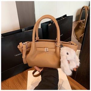 Detailed close-up of caramel lychee grain leather bucket bag with plush rabbit charm
