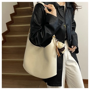 Détail du sac fourre-tout crème avec breloque ours, présenté sur mannequin en extérieur