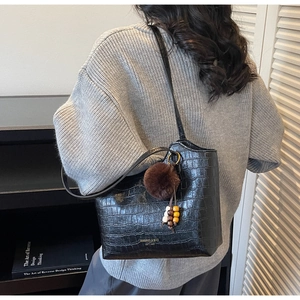Detail view of black crocodile pattern bucket bag with a decorative faux fur charm