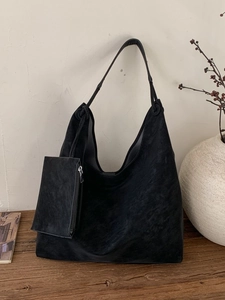Minimalist black suede hobo bag with matching mini pouch on a rustic wooden desk