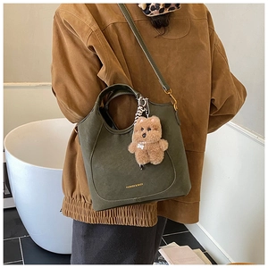 Detail of dark green suede bucket bag featuring gold lettering and brown teddy bear charm