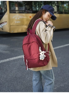 Close-up of red plaid backpack with white bear keychain and tassel on city street