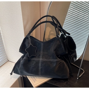 Detail of black matte leather tote bag featuring white contrast stitching and star tag