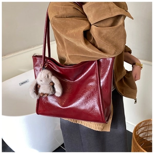 Detail of burgundy large tote bag with glossy leather texture and plush rabbit charm