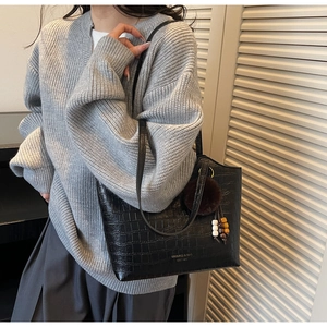 Detail of black crocodile texture tote bag with plush charm on a model's shoulder