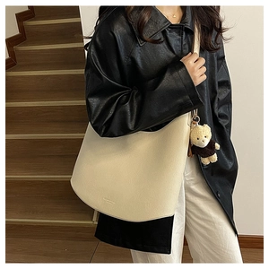 Détail d'un sac bandoulière en cuir crème avec charm ours porté par un mannequin