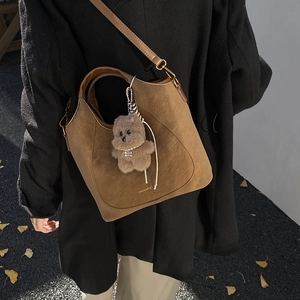 Brown suede hobo bag with a plush bear charm showing on a model in a seasonal setting