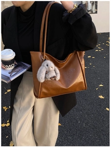 Brown leather tote bag detail with cute bunny charm carried by model on street