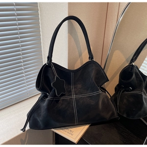 Detail of black suede tote bag with white cross stitching and star pendant charm