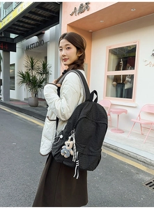 Detail of checkered backpack with plush bear charm and striped lanyard on street model