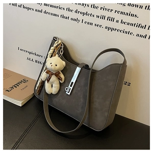 Detail of grey suede underarm bag with silver buckle and cute white teddy bear charm