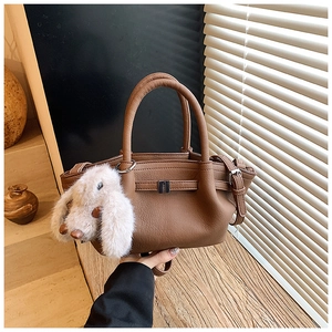 Detailed view of a brown pebbled leather bucket bag with a cute white bunny plush pendant